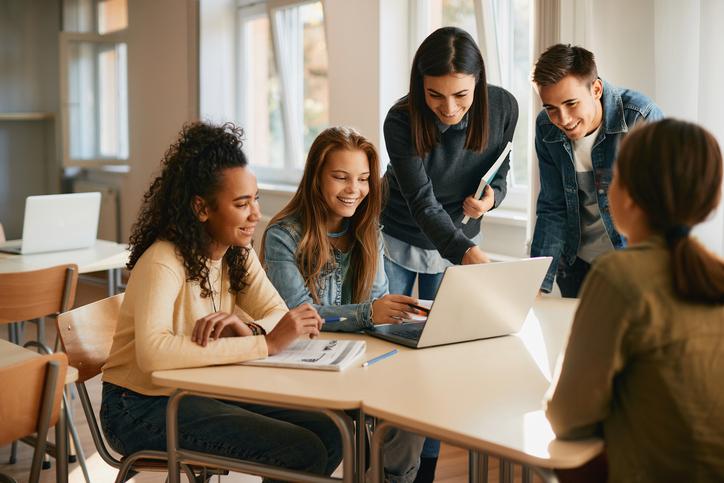 Students and support staff work together round a laptop
