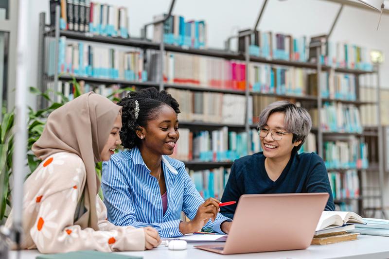 Three female students in library around laptop