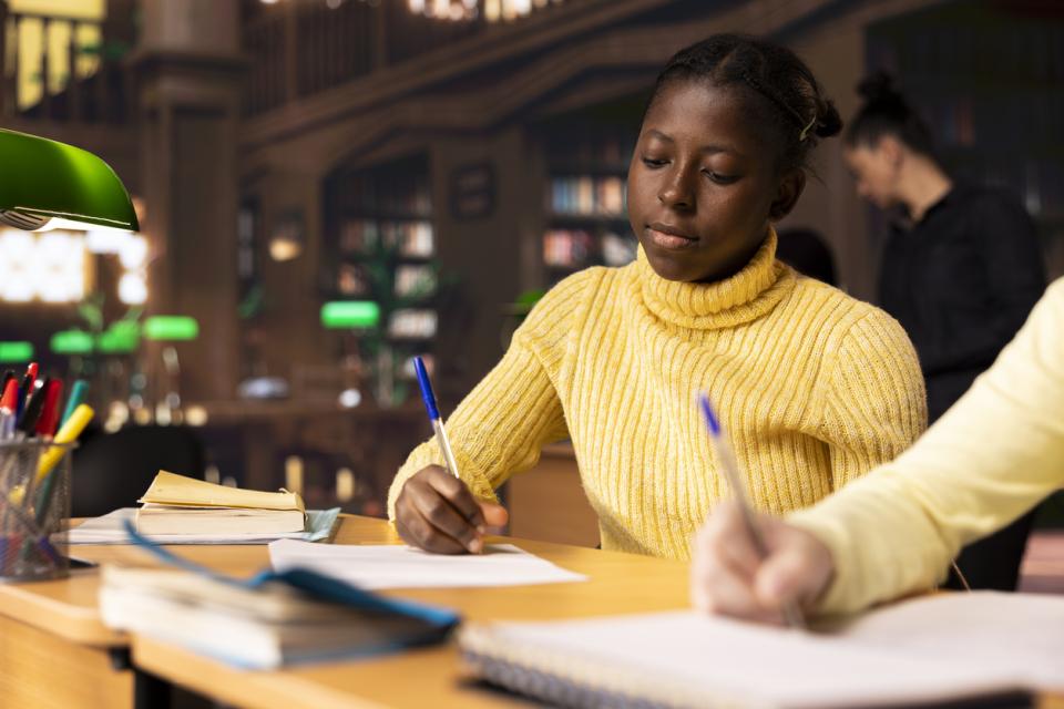 A student writing an essay by hand in a library