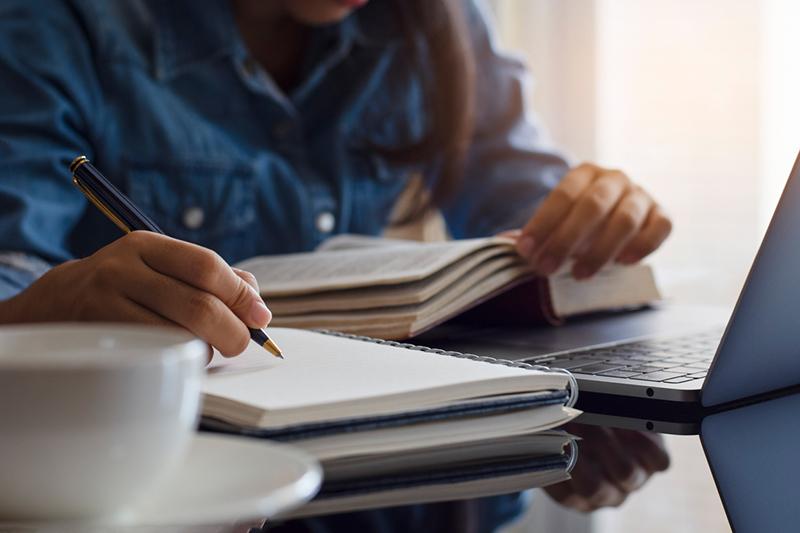 Young woman writing notes with a pad and laptop