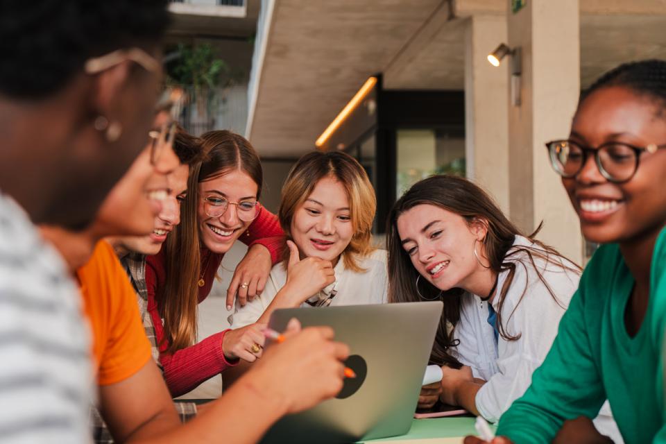 A group of students interacting happily around a laptop
