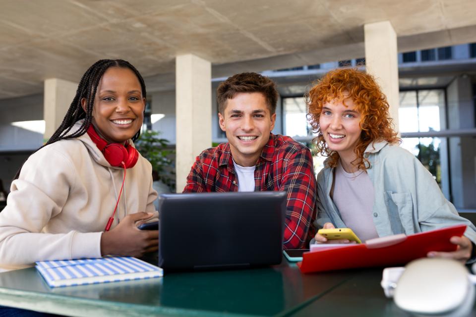 Three students working from a laptop smiling to camera