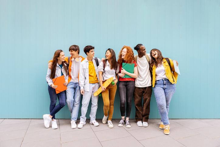 Students laugh together in front of a blue wall