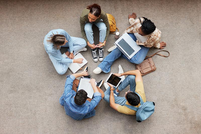 Students sitting in a circle on the floor with laptops
