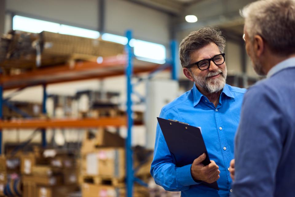 A businessman in a warehouse speaks to a business partner.