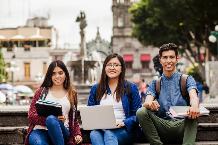 Three international students sitting in front of a landmark