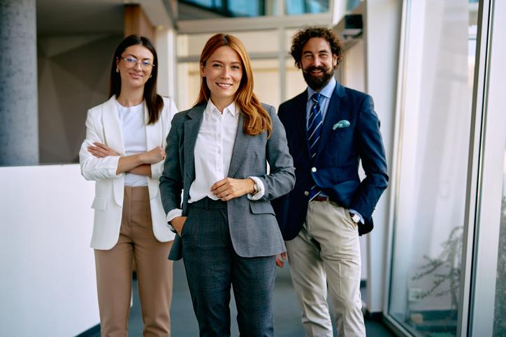 Three business professionals standing in an office and smiling to camera