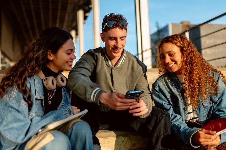 University students sitting outside looking at a funny video on one of their phones