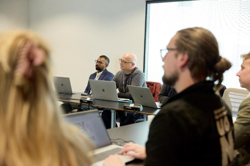 University staff on laptops listening to a speaker out of shot