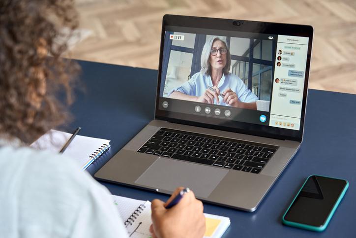 A student watches a teacher lecture on a laptop