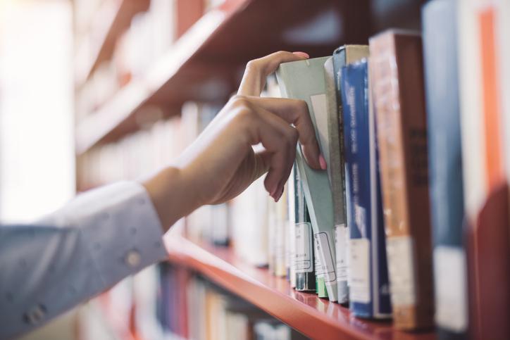 A hand pulling out a book from a library shelf