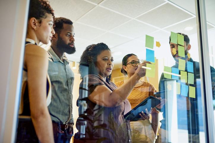 Staff and students strategising with Post-It notes on a transparnt screen
