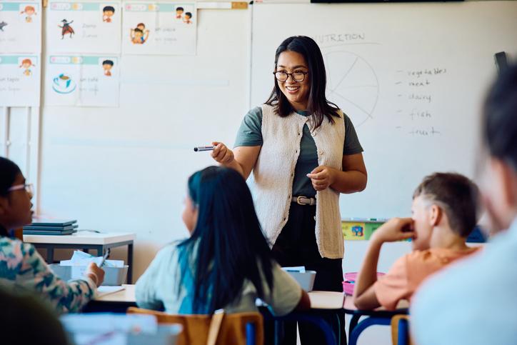 A schoolteacher standing in front of a whiteboard interacting with pupils