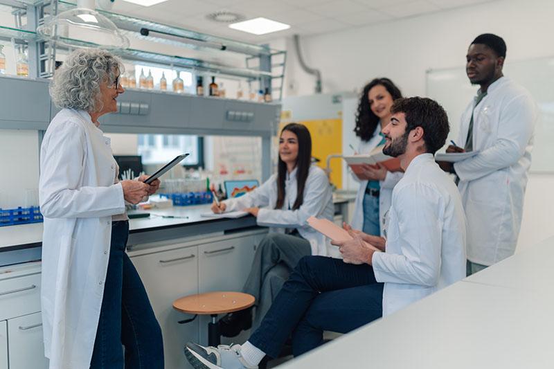 Diverse group of young adult students listening to their mature female professor during a chemistry lecture in a lab