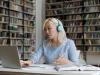Young Asian woman working at laptop in library wearing headphones