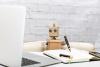 A small toy robot works at a notebook with a laptop open
