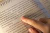 A finger follows text in a book written in question marks