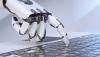 A robot hand presses a key on a laptop keyboard