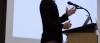 A lecturer stands in front of a microphone