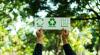 Hands holding up a sign that says "reuse", "recycle" and "reduce" with accompanying icons