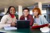 Three students working from a laptop smiling to camera