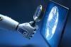 Robot hand holding magnifying glass up to computer screen