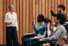 A professor explaining course structure to a class full of students, some of whom have their hands raised